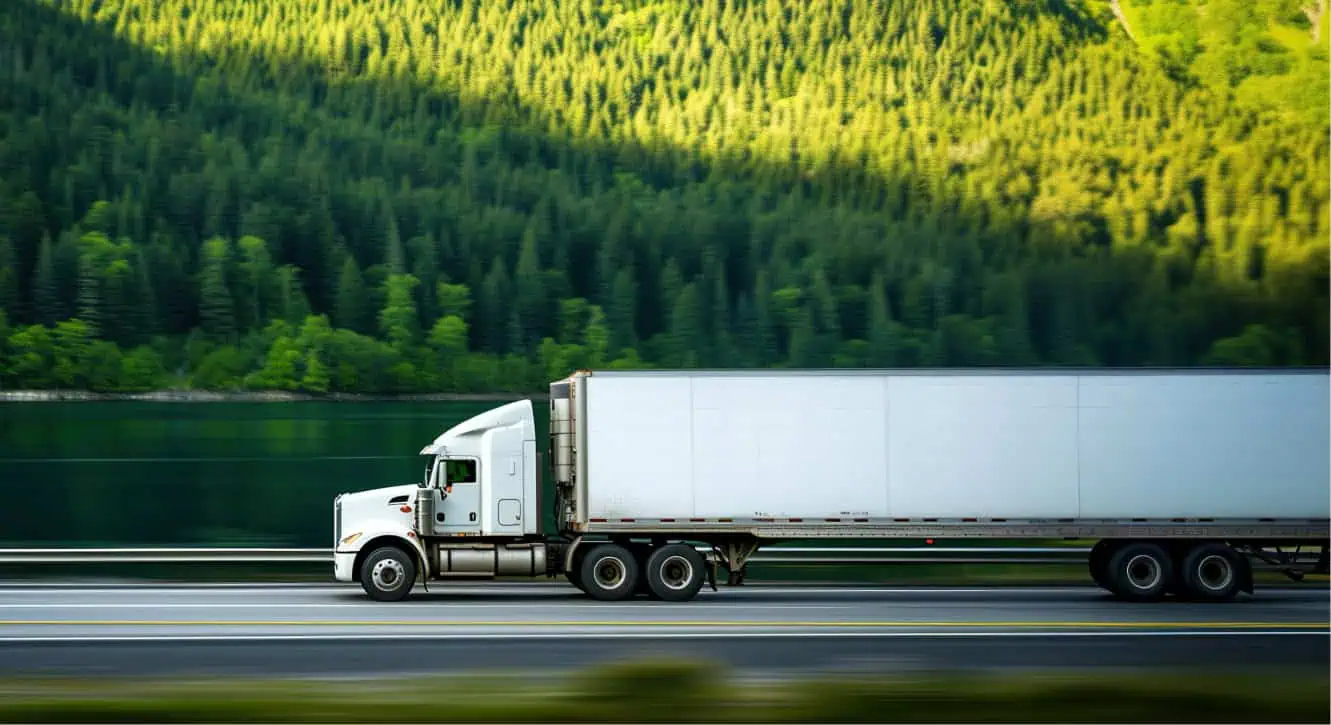 white freight truck on highway with trees in background