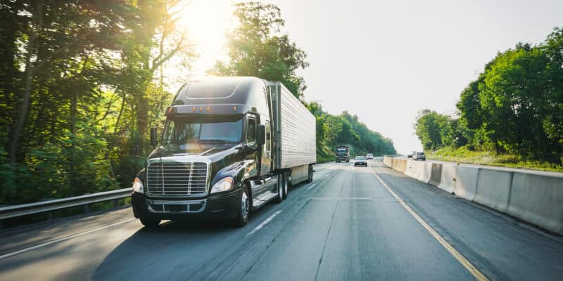 Freight truck driving on a road with sunshine in the background